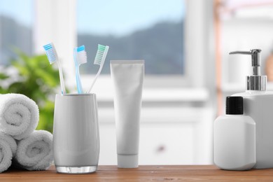 Photo of Plastic toothbrushes in holder, cosmetic products and towels on wooden table indoors