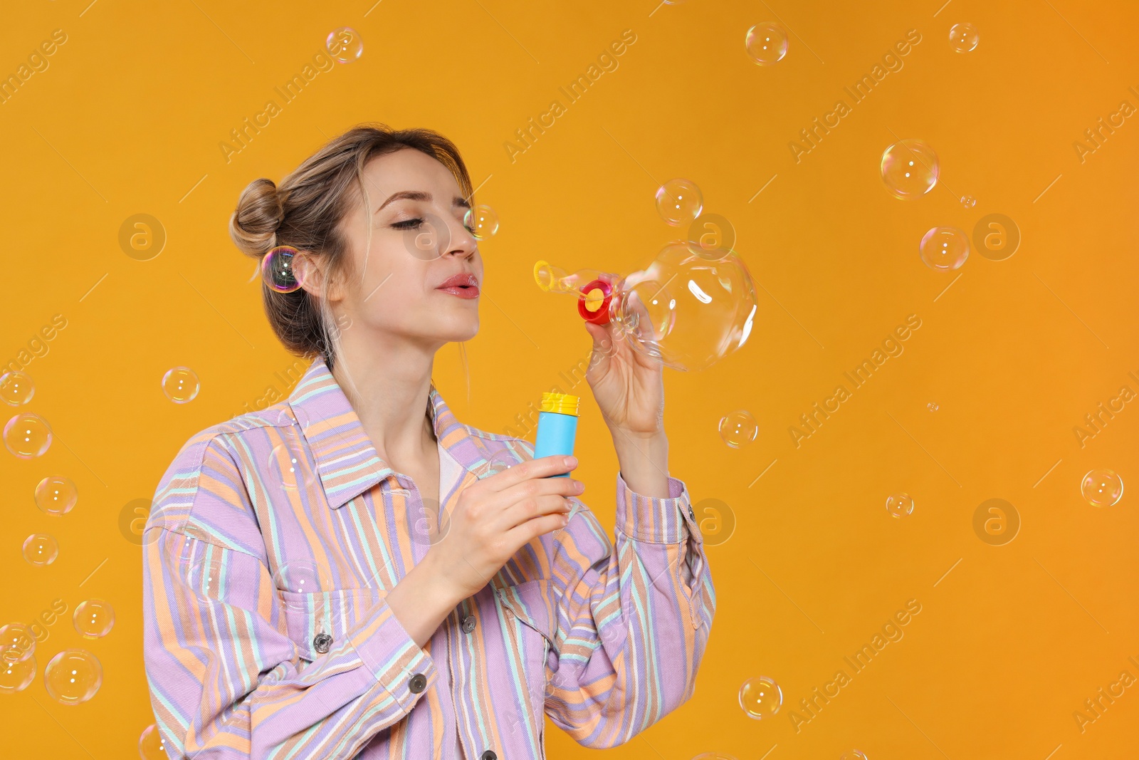 Photo of Young woman blowing soap bubbles on yellow background, space for text