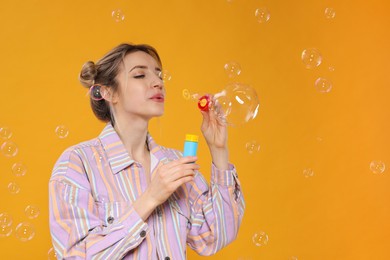 Photo of Young woman blowing soap bubbles on yellow background, space for text