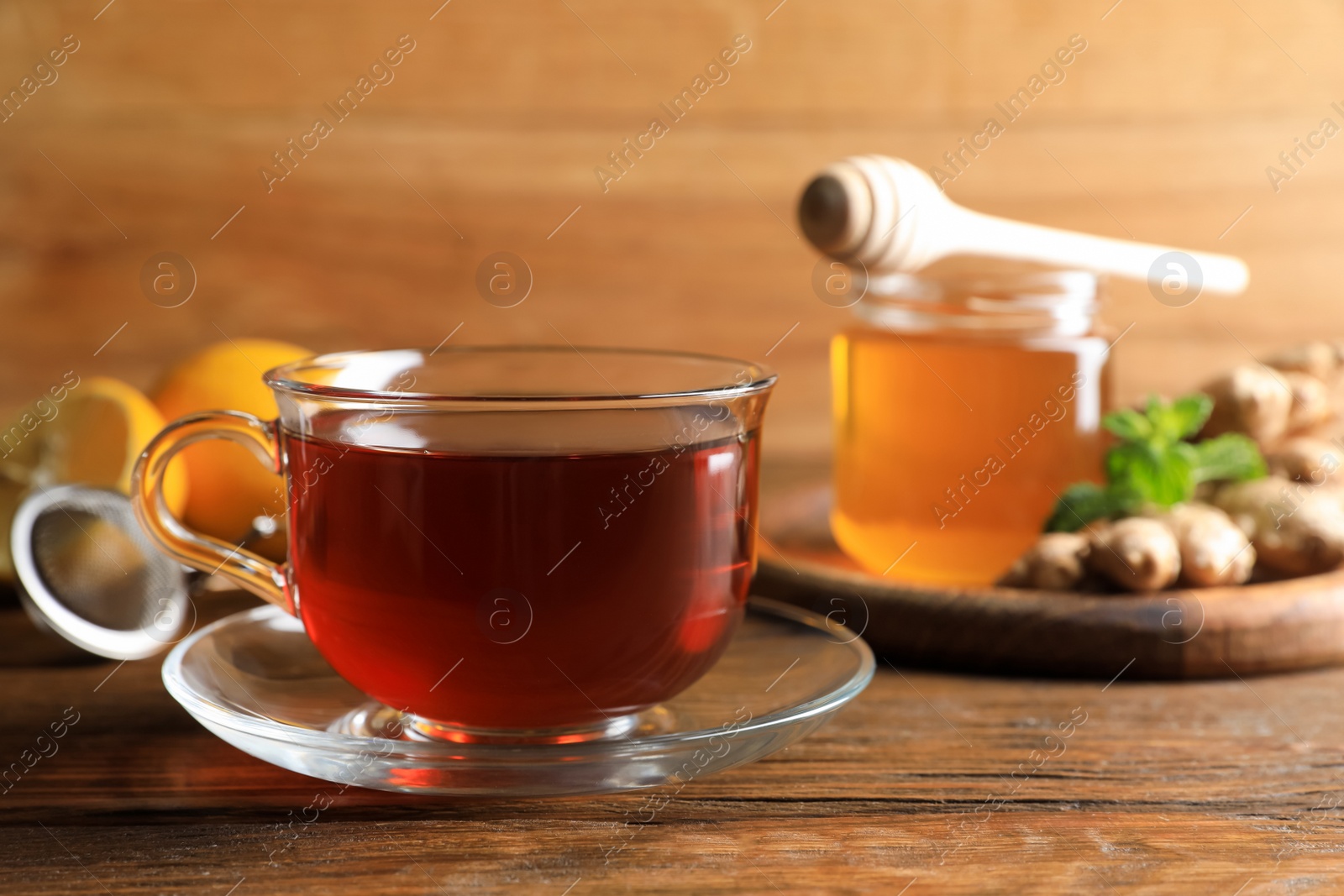 Photo of Cup of delicious ginger tea and ingredients on wooden table