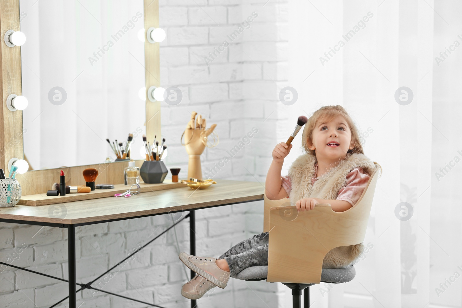 Photo of Cute little girl playing with cosmetics in dressing room