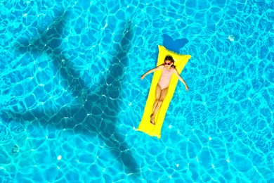 Shadow of airplane and girl on inflatable mattress in swimming pool, top view. Summer vacation