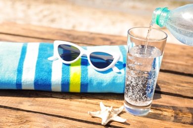 Photo of Pouring refreshing drink into glass on wooden deck with beach accessories. Hot summer day