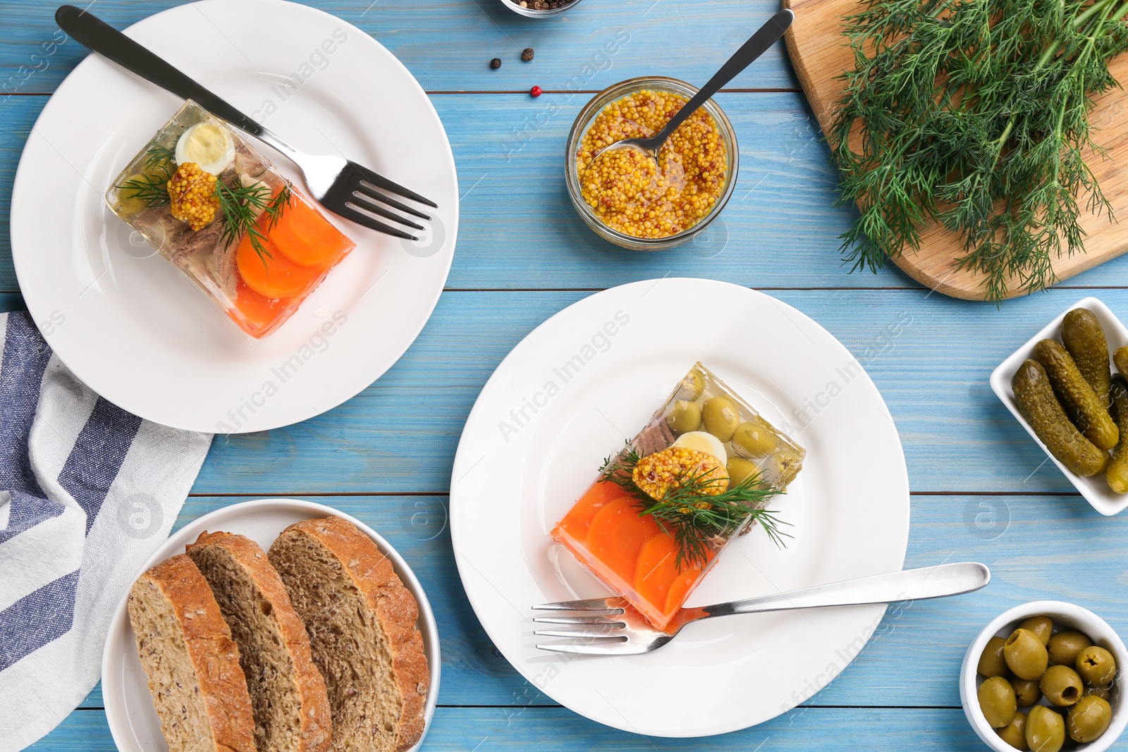 Photo of Delicious aspic with meat and vegetables served on light blue wooden table, flat lay