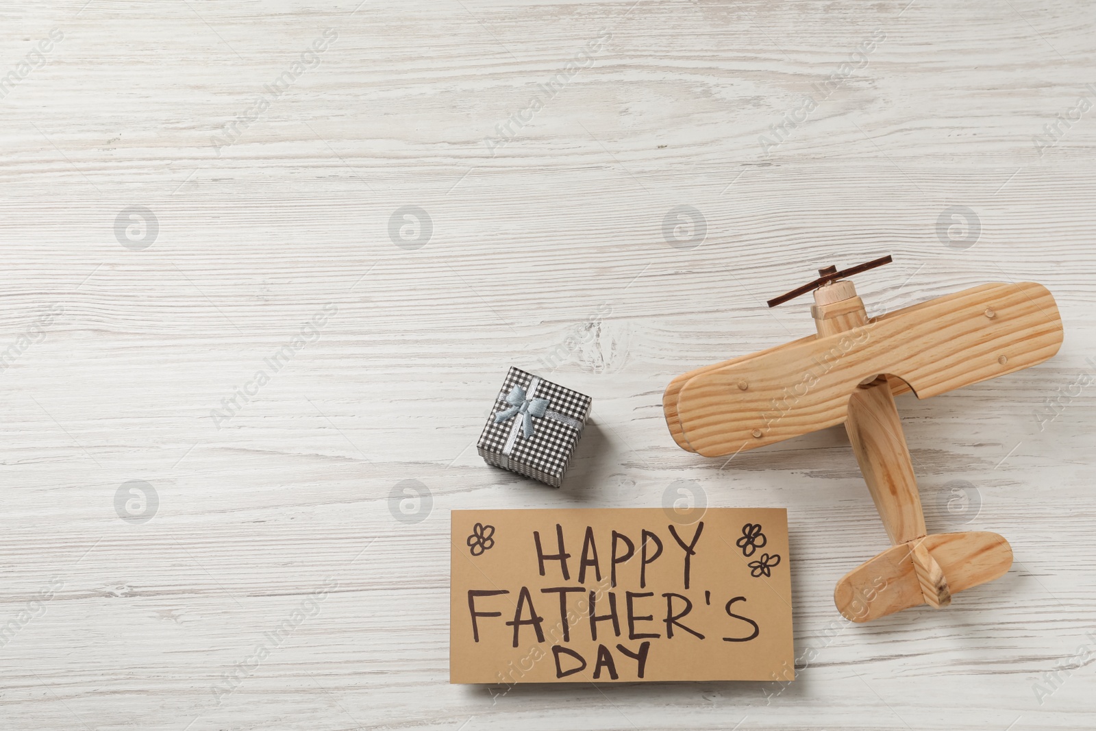 Photo of Card with phrase Happy Father's Day, toy plane and gift box on white wooden background, flat lay. Space for text