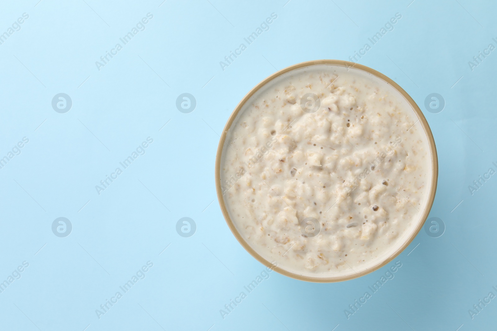 Photo of Tasty boiled oatmeal in bowl on light blue table, top view. Space for text