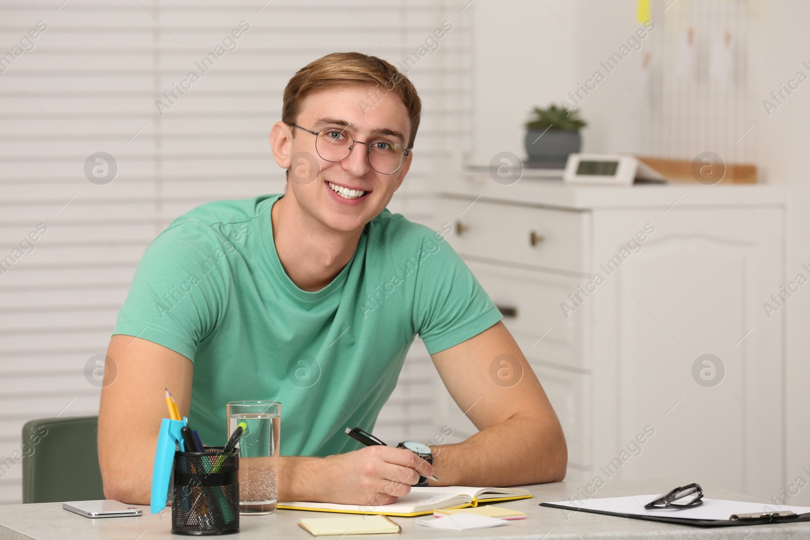 Photo of Young man writing in notebook at table indoors