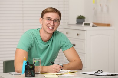 Young man writing in notebook at table indoors