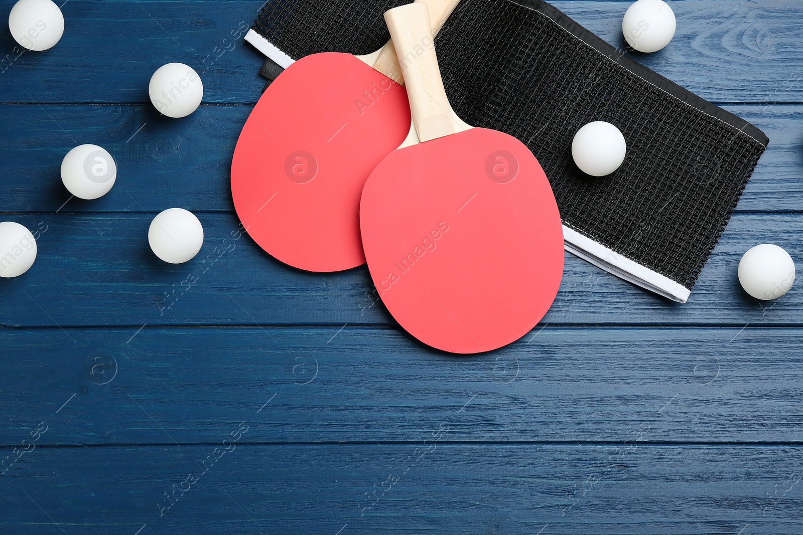 Photo of Ping pong rackets, net and balls on blue wooden table, flat lay. Space for text