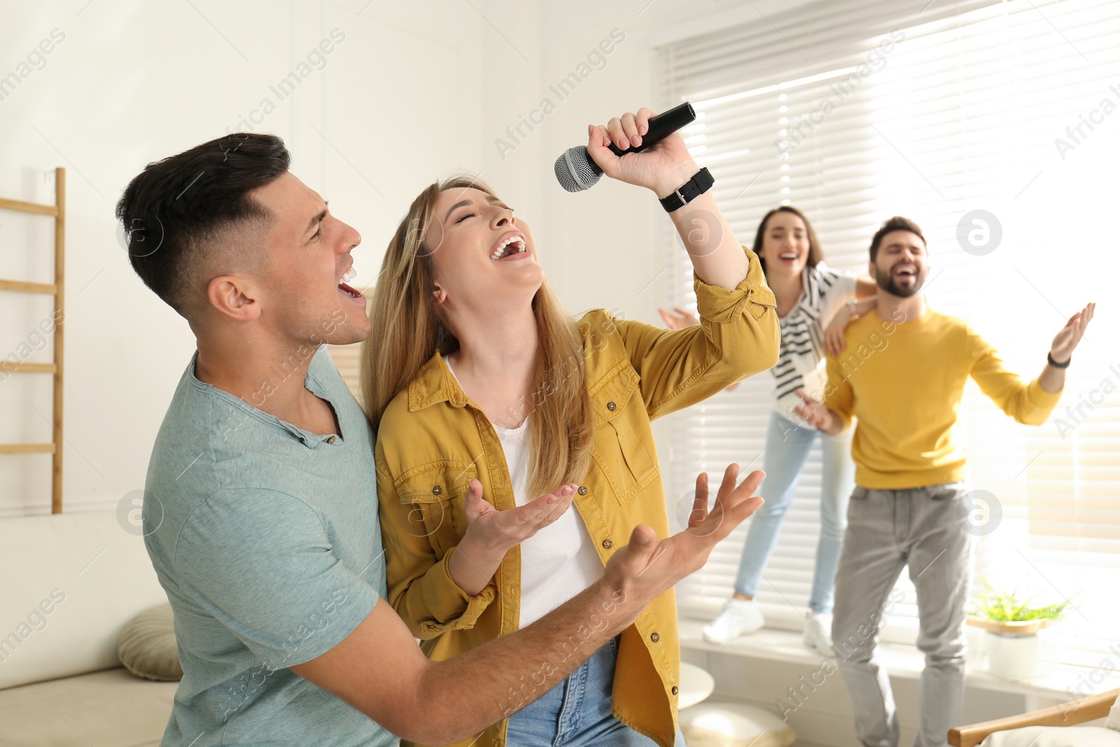 Photo of Happy couple singing karaoke with friends at home