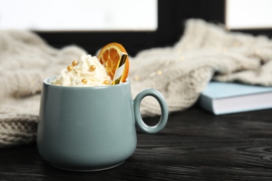 Photo of Cup of winter drink with whipped cream and knitted scarf on window sill