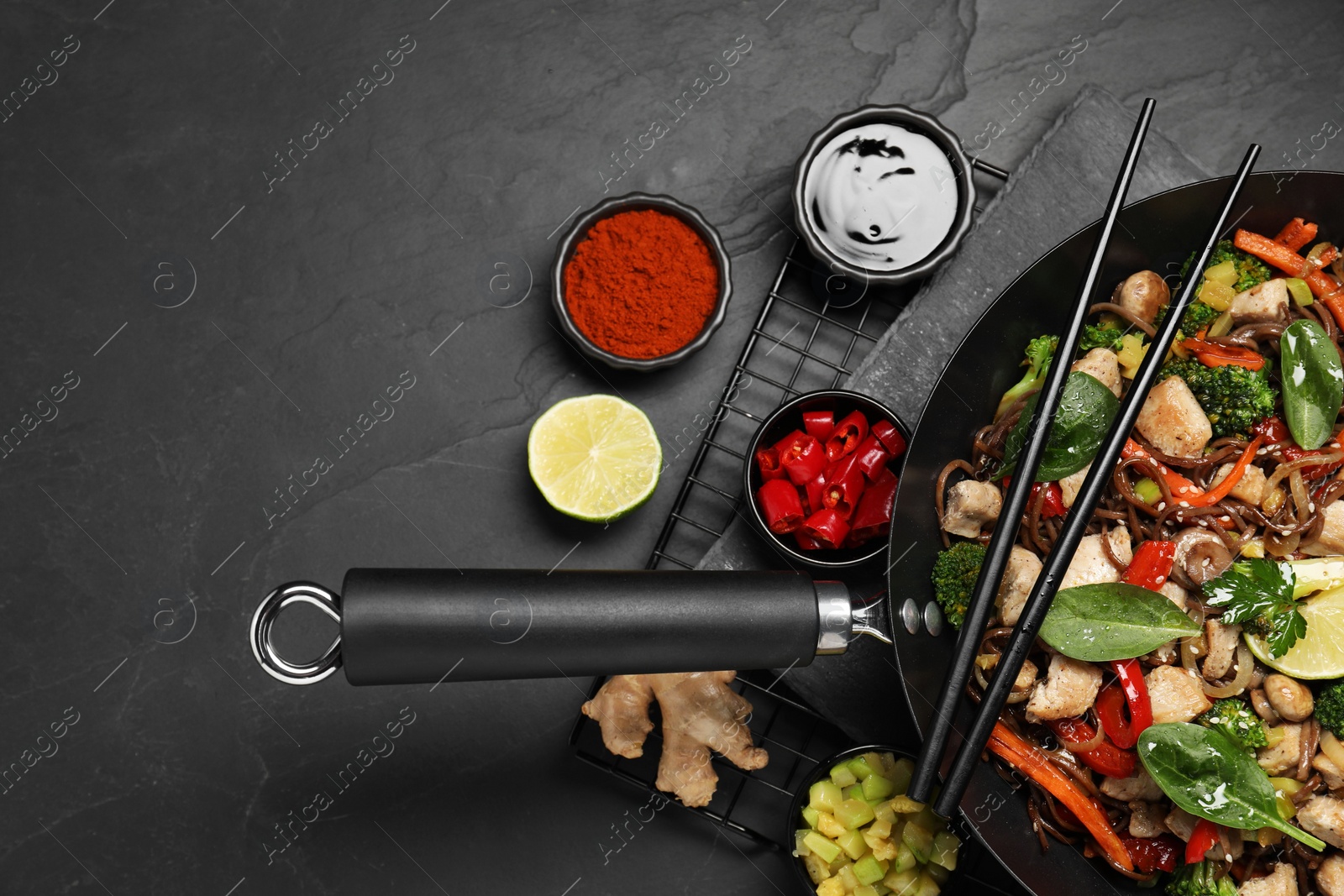 Photo of Stir-fry. Tasty noodles with meat in wok, chopsticks and ingredients on grey textured table, flat lay