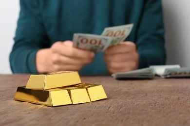 Photo of Person counting money at table, focus on stacked gold bars. Space for text