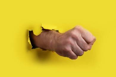 Man breaking through yellow paper with fist, closeup