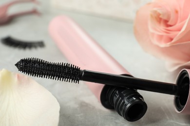 Photo of Mascara for eyelashes and flower on light background, closeup. Makeup product