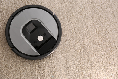 Modern robotic vacuum cleaner on beige carpet, top view. Space for text