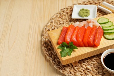 Delicious sashimi set of salmon and shrimps served with cucumbers, parsley, wasabi and soy sauce on wooden table. Space for text