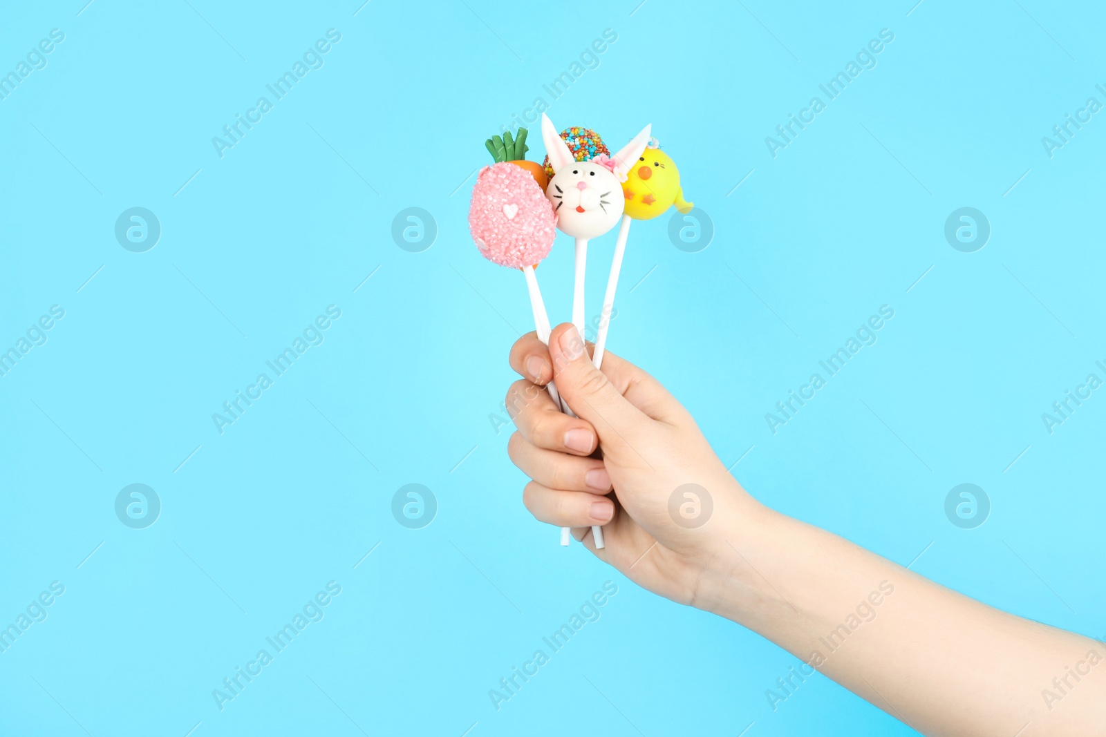 Photo of Woman with delicious cake pops on light blue background, closeup. Easter holiday