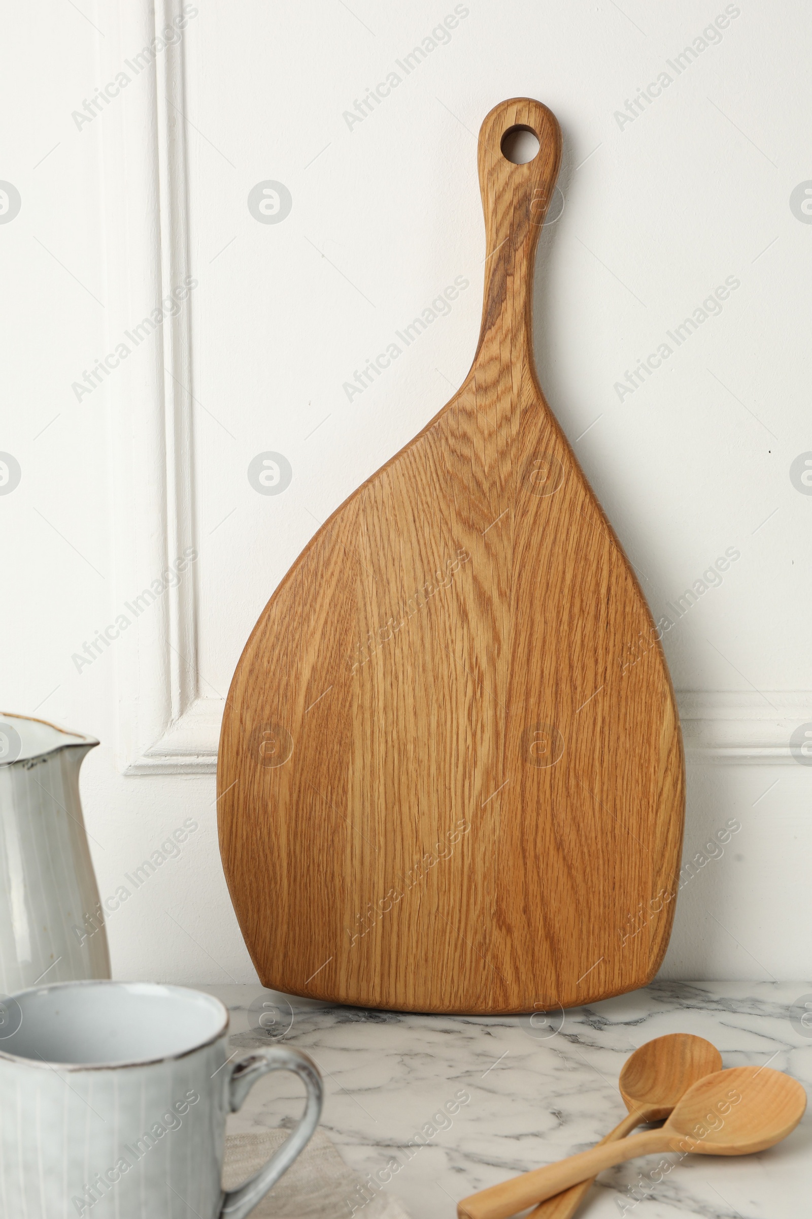 Photo of Wooden cutting board, spoons and dishware on white marble table