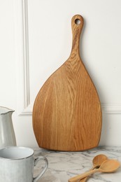 Wooden cutting board, spoons and dishware on white marble table