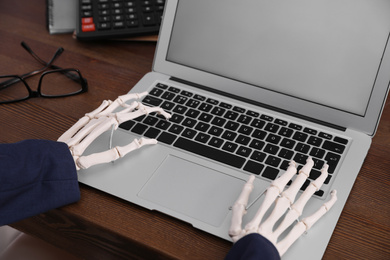 Human skeleton in suit using laptop at table, closeup