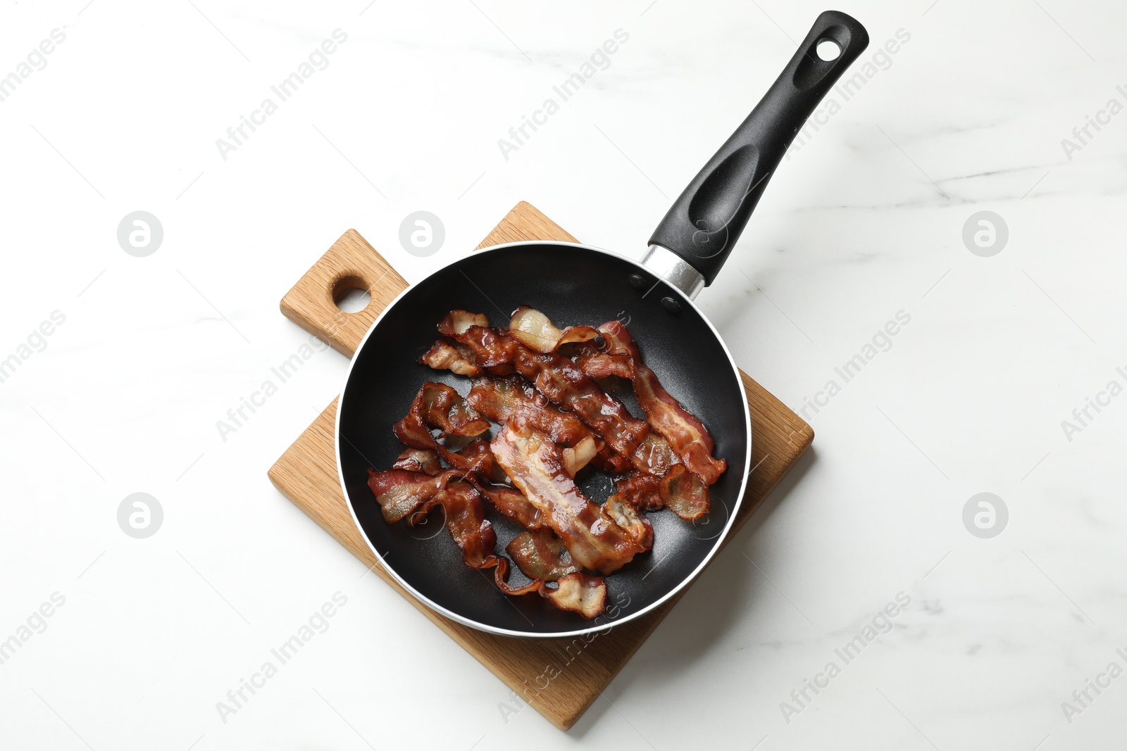 Photo of Delicious bacon slices in frying pan on white marble table, top view