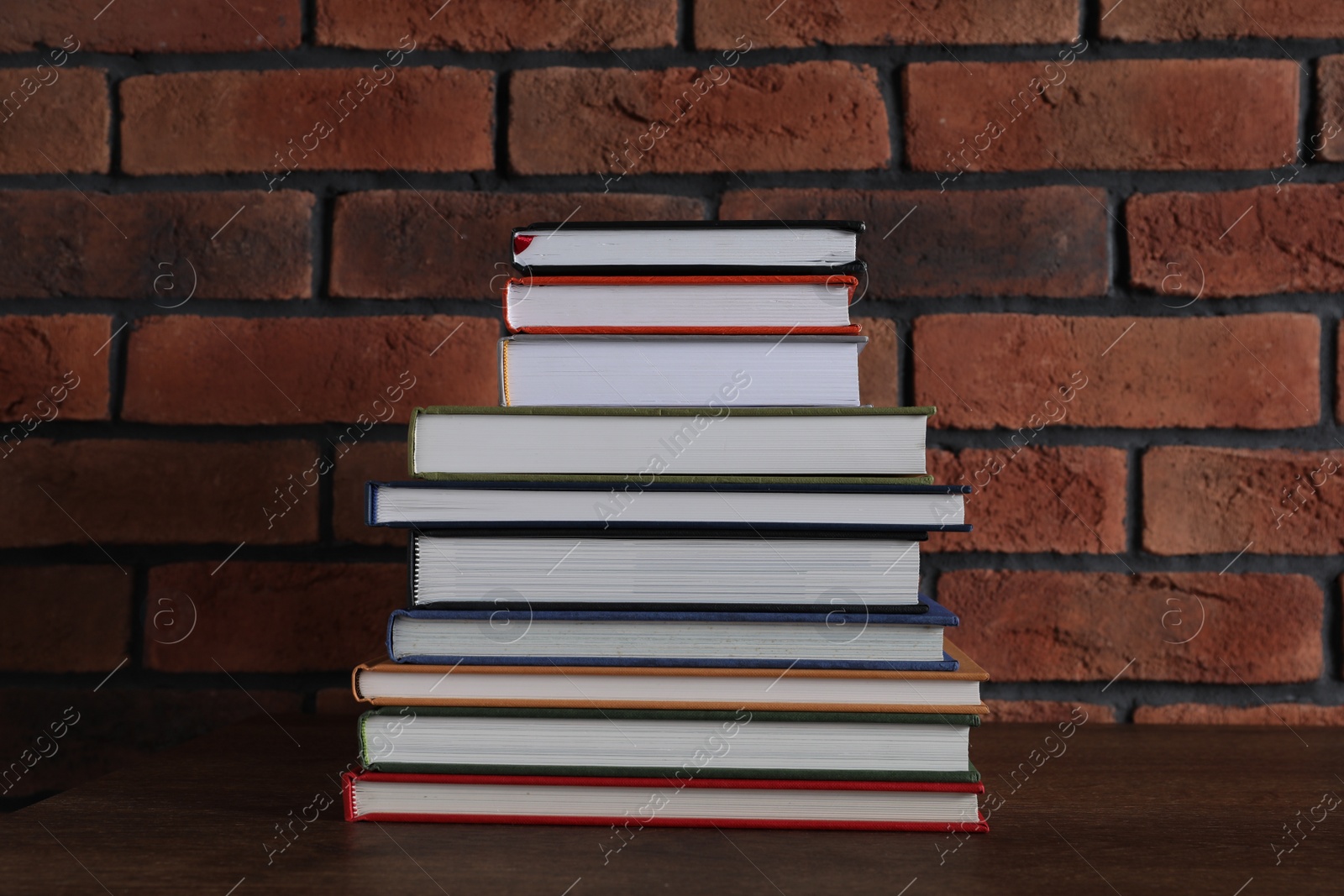 Photo of Stack of hardcover books on wooden table near brick wall