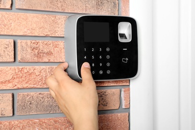 Young man entering code on alarm system keypad indoors