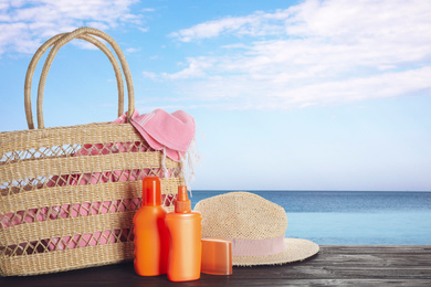 Image of Set of sun protection products and stylish accessories on wooden table near sea