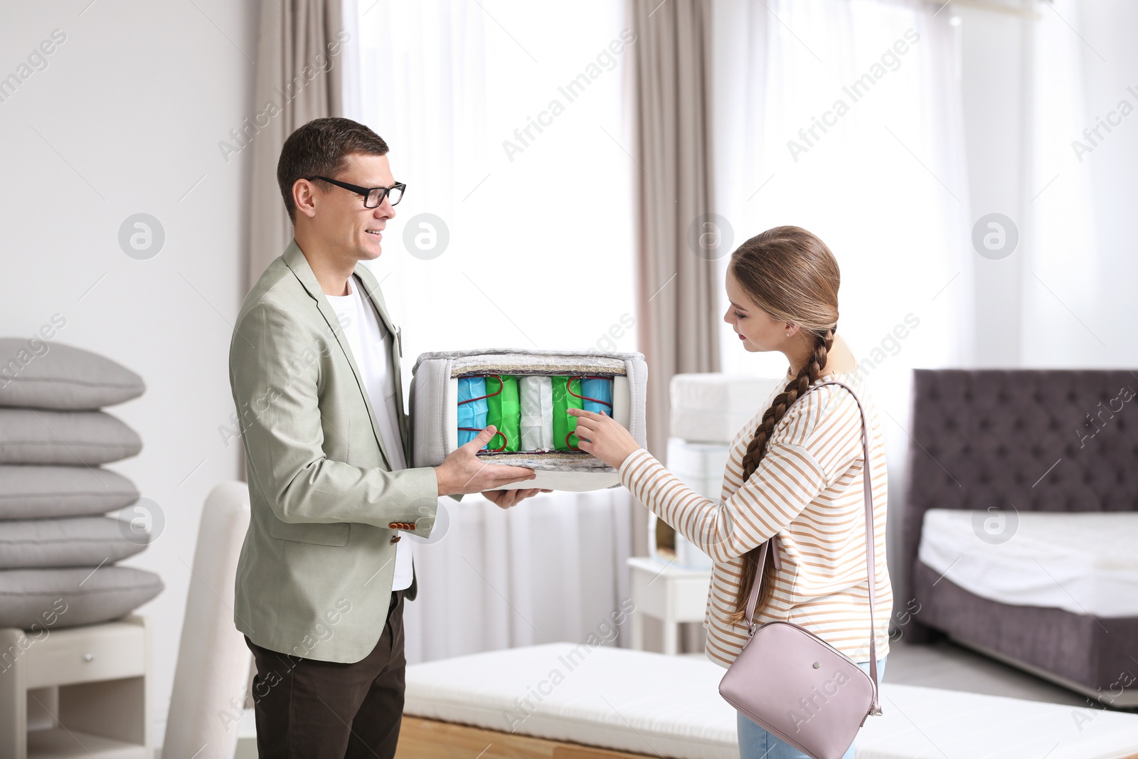 Photo of Salesman showing young woman section of mattress in store