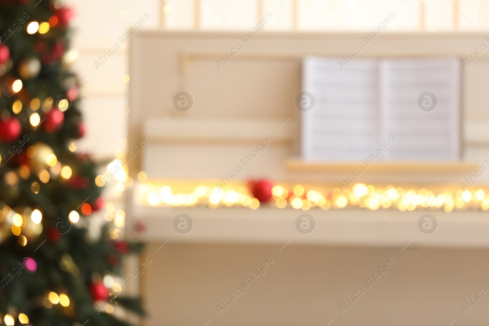 Photo of Blurred view of white piano with fairy lights indoors. Christmas music