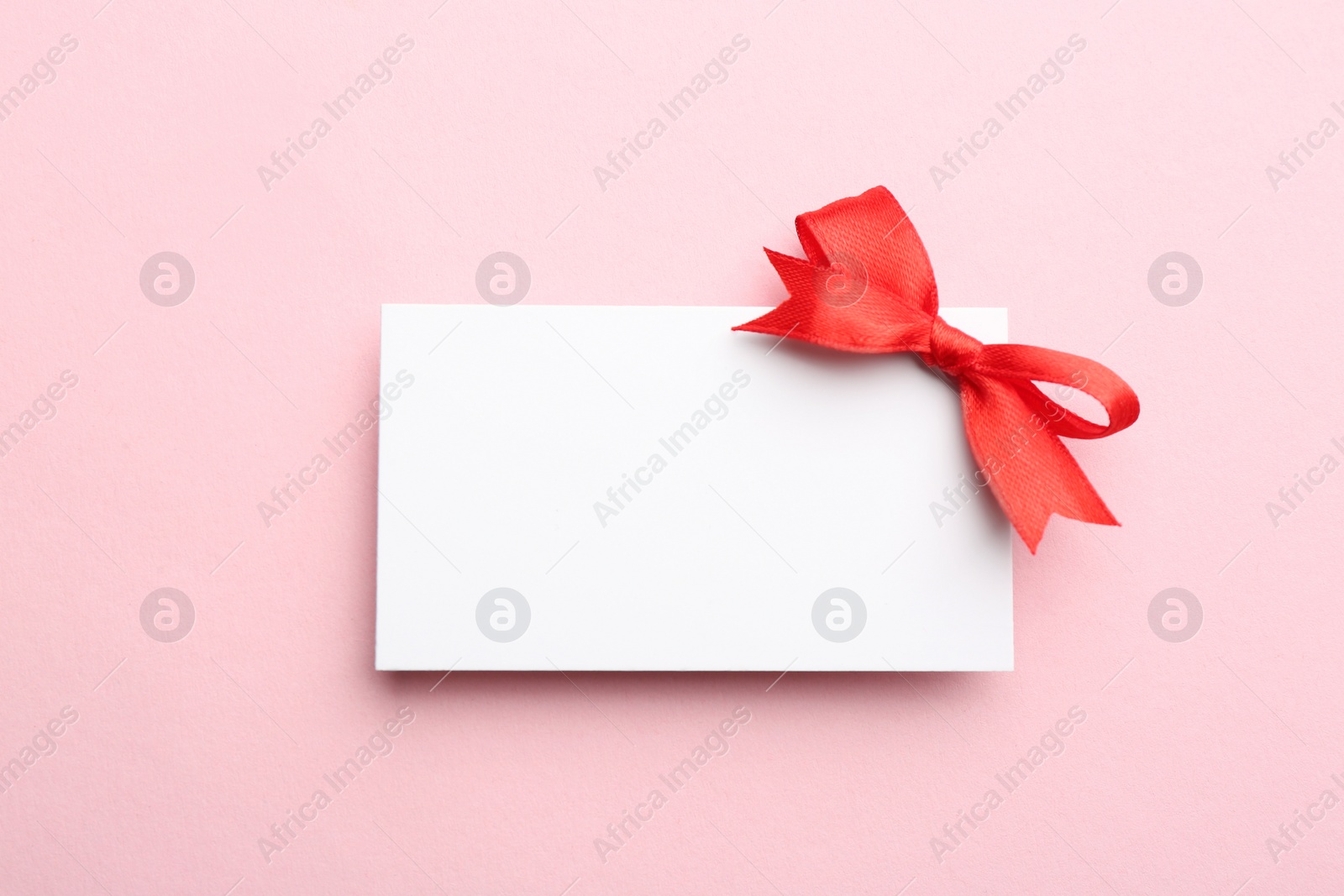 Photo of Gift card with bow on pink background, top view. Mockup for design