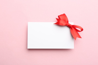 Photo of Gift card with bow on pink background, top view. Mockup for design