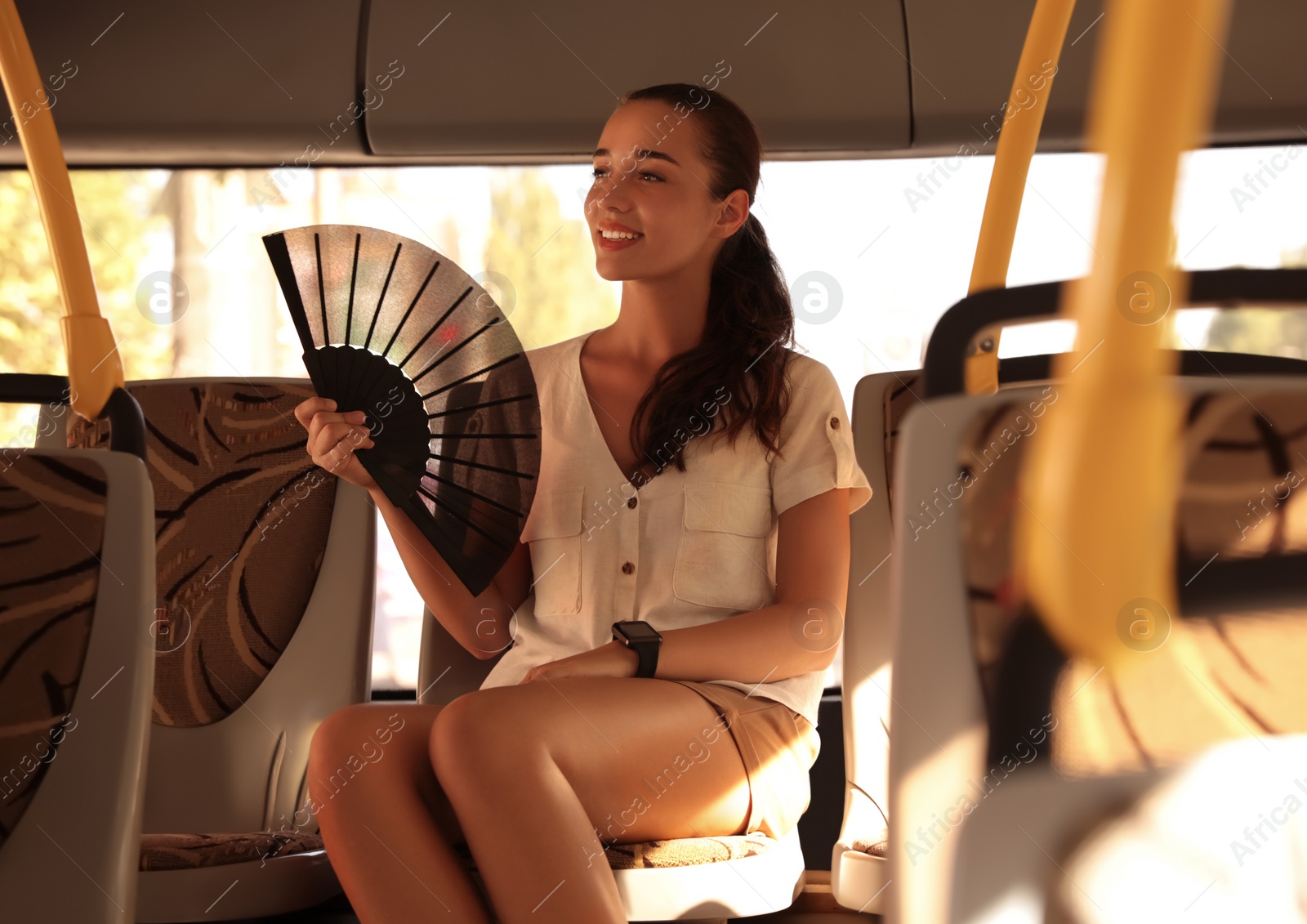 Photo of Young woman using hand fan in bus on hot summer day