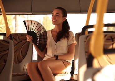 Photo of Young woman using hand fan in bus on hot summer day