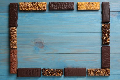 Photo of Frame of different tasty protein bars on light blue wooden table, flat lay. Space for text