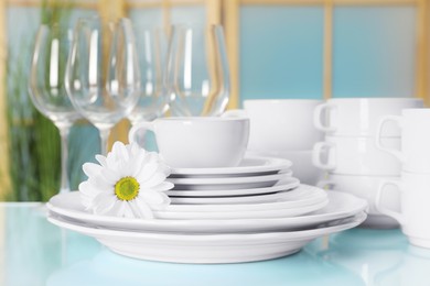 Set of clean dishware and flower on light blue table, closeup