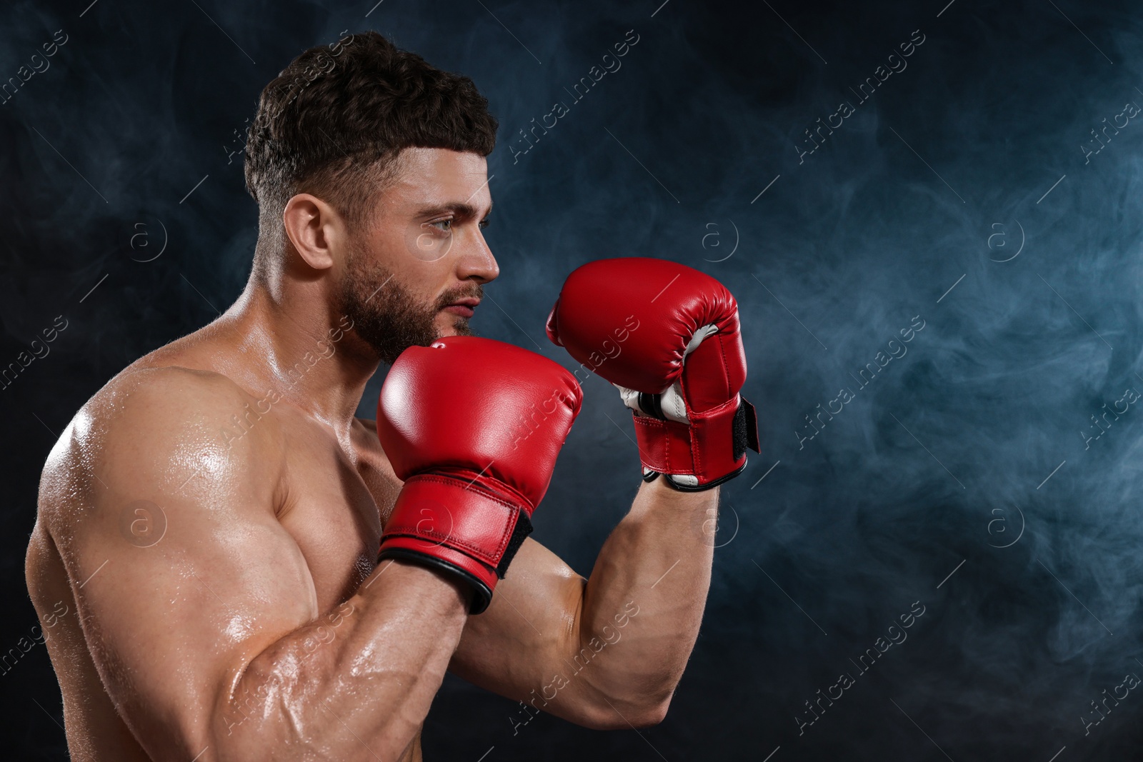 Photo of Man wearing boxing gloves fighting in smoke on black background. Space for text