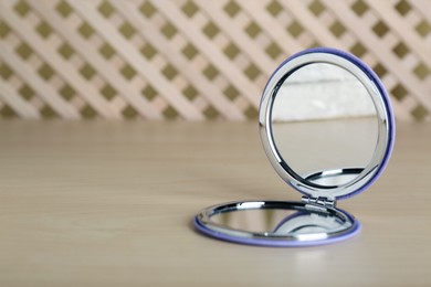 Photo of Stylish cosmetic pocket mirror on wooden table. Space for text