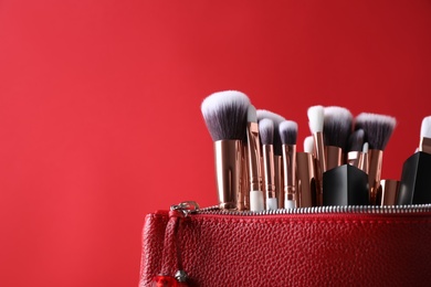 Photo of Bag with makeup brushes and cosmetic products on red background. Space for text