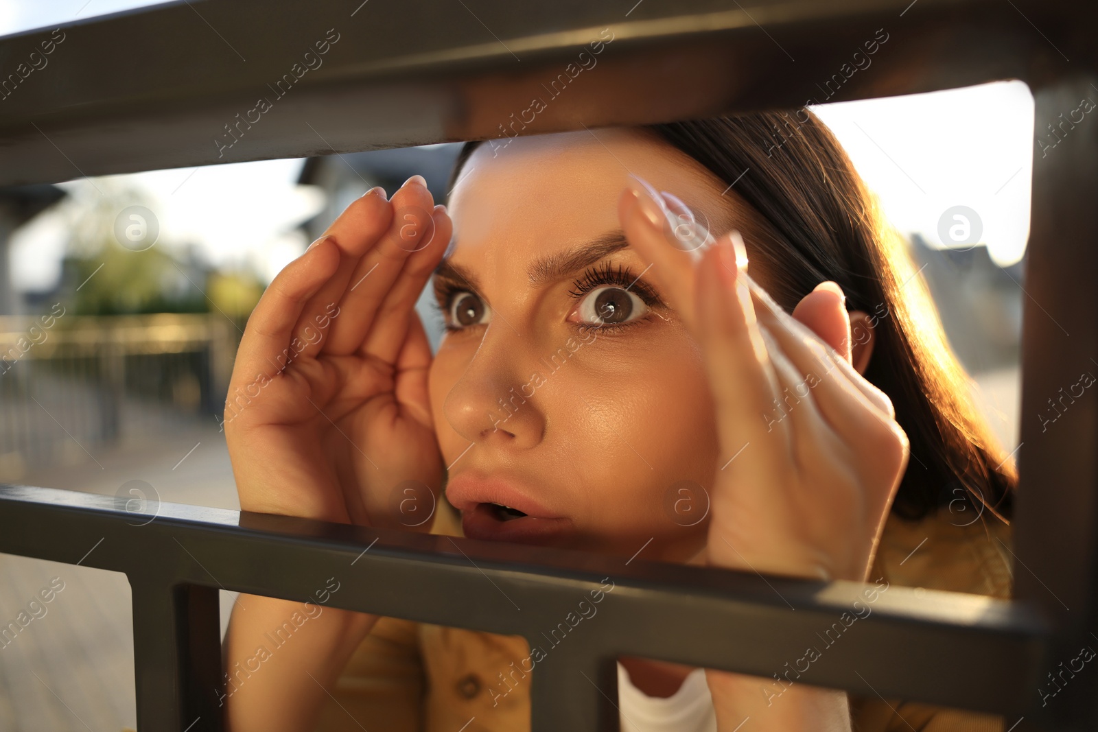 Photo of Concept of private life. Curious young woman spying on neighbours over fence outdoors, closeup