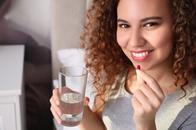 Photo of African-American woman with glass of water taking vitamin pill at home