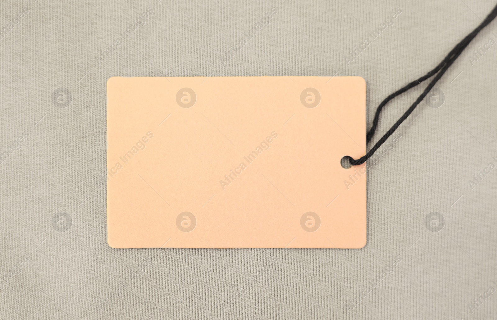 Photo of Cardboard tag on beige garment, top view. Space for text