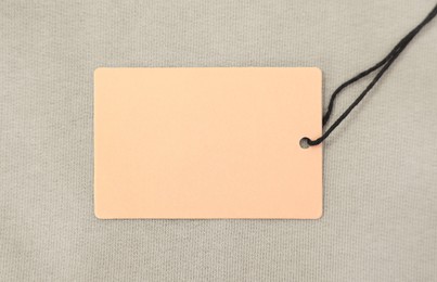 Photo of Cardboard tag on beige garment, top view. Space for text