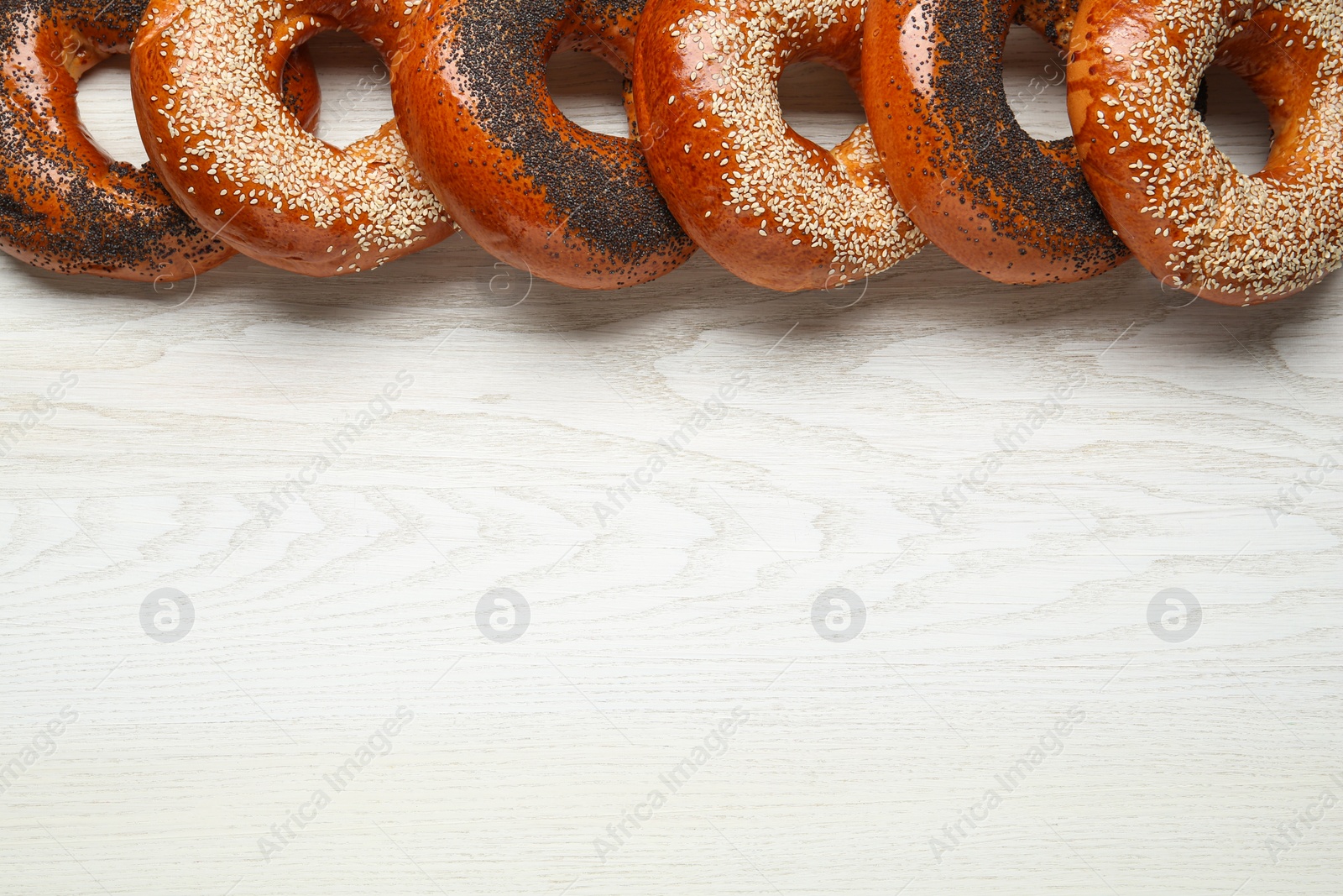 Photo of Many delicious fresh bagels on white wooden table, flat lay. Space for text