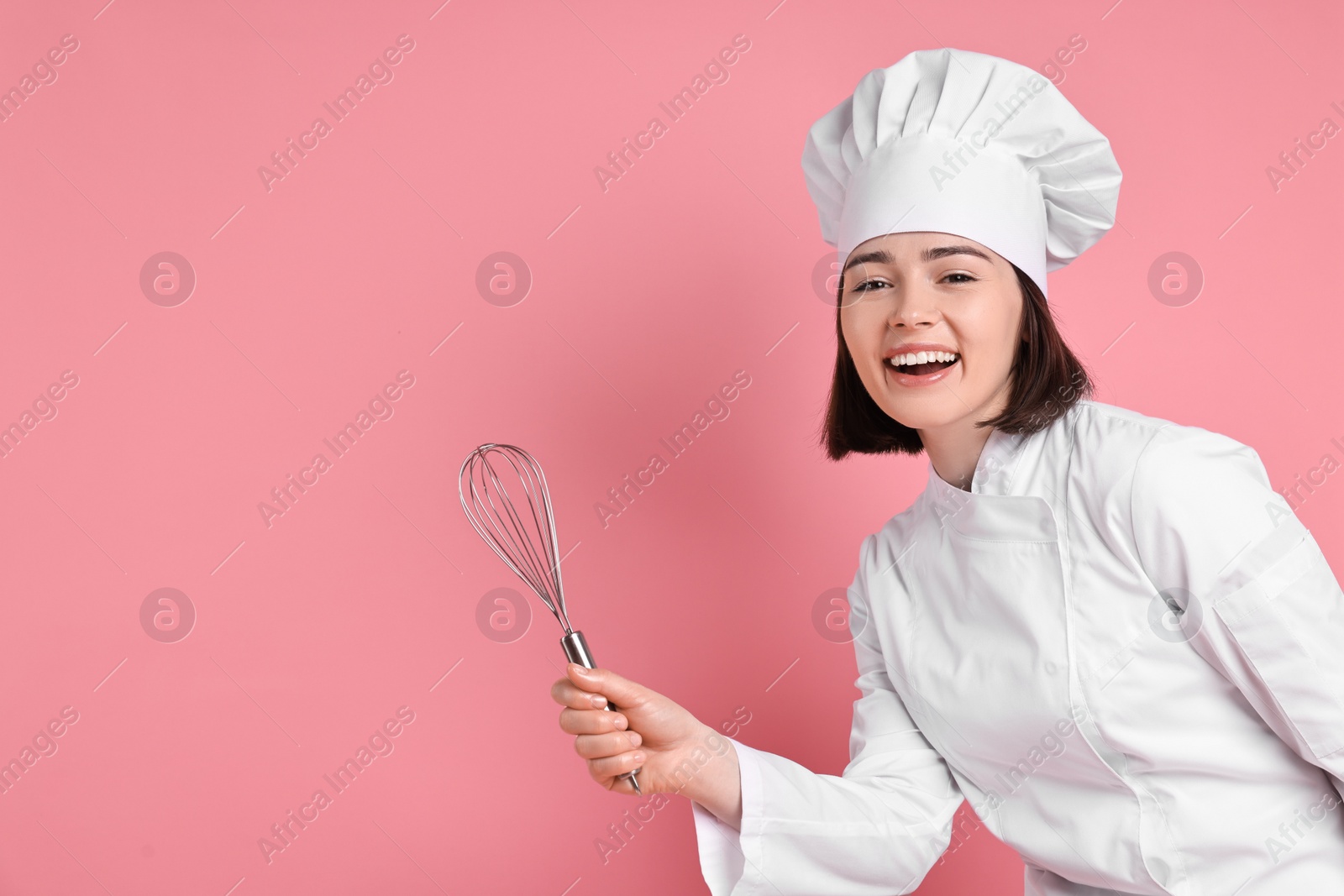 Photo of Happy confectioner with whisk on pink background, space for text