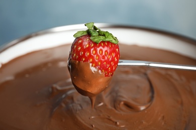 Photo of Dipping strawberry into pot with tasty chocolate fondue, closeup