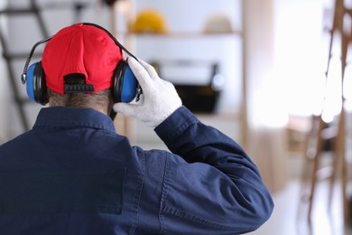 Photo of Worker wearing safety headphones indoors, back view. Hearing protection device