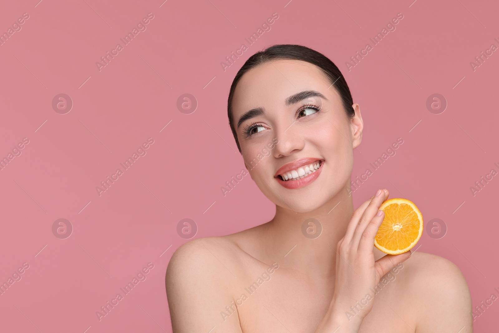 Photo of Beautiful young woman with piece of orange on pink background. Space for text