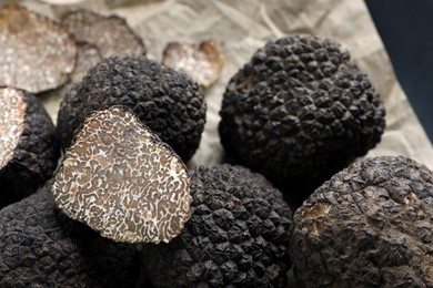 Photo of Whole and cut black truffles on parchment, closeup